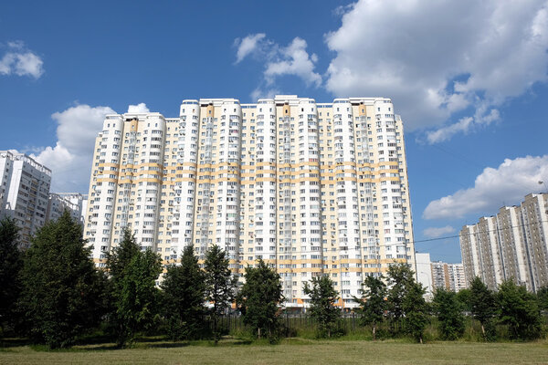 Facade of high modern beige residential buildings on blue sky with white clouds