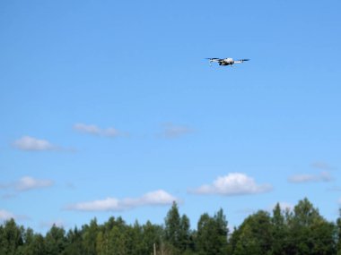 Mavi gökyüzünün altında, açık beyaz bulutlarla aydınlık güneşli yaz gününde, orman ağaçlarının üzerinde uçan drone 'lar.