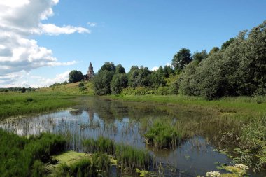 Önünde hala gölet olan güzel sessiz kırsal alan, aydınlık yaz gününde gökyüzünde eski kilise ve bulutlar.