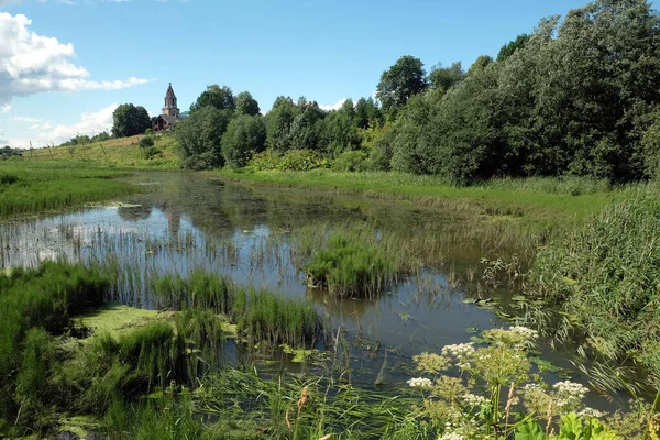 Önünde hala gölcükler olan güzel, sessiz, kırsal bir arazi, uzak bir yerde eski bir kilise ve açık bir yaz gününde gökyüzünde bulutlar.