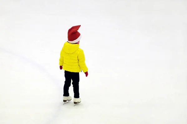 冬服の小さな子供と赤い新年の帽子はスケートリンクの氷の上に立つバックビュー — ストック写真