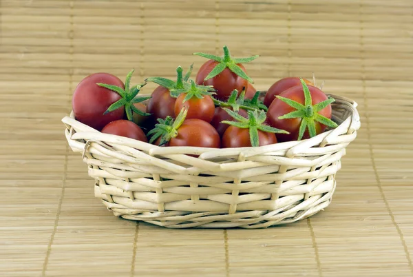Tomates rojos en canasta de mimbre sobre estera de paja — Foto de Stock