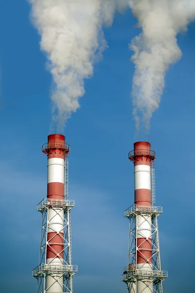 Two striped industrial pipes with smoke over cloudless blue sky — Stock Photo, Image