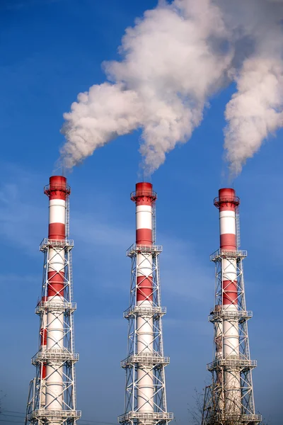 Три полосатые промышленные трубы с дымом над безоблачным голубым небом — стоковое фото