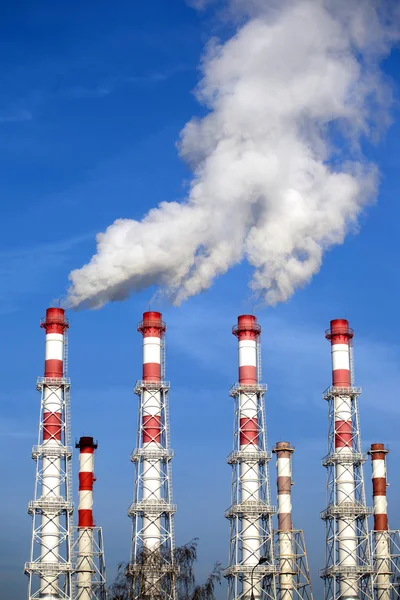 Tuyaux industriels avec fumée blanche sur ciel bleu. Photo verticale — Photo