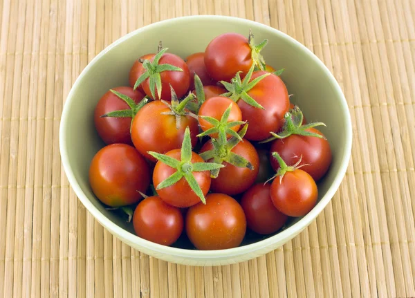 Red tomatoes in green bowl on straw mat — Stock Photo, Image