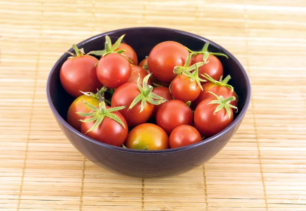 Red tomatoes in violet bowl on straw mat — Stock Photo, Image