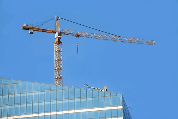 Guindaste de torre no topo do edifício arranha-céus de construção sobre céu azul sem nuvens — Fotografia de Stock