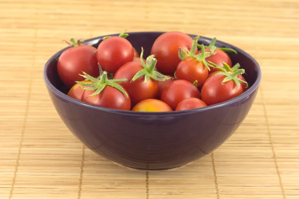 Tomates rouges dans un bol violet sur un tapis de paille — Photo