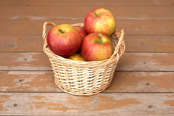Apples in light brown wicker basket on old wooden desk closeup — Stock Photo, Image