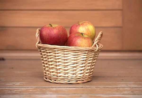 Яблоки в светло-коричневой плетеной корзине на деревянном столе крупным планом — стоковое фото