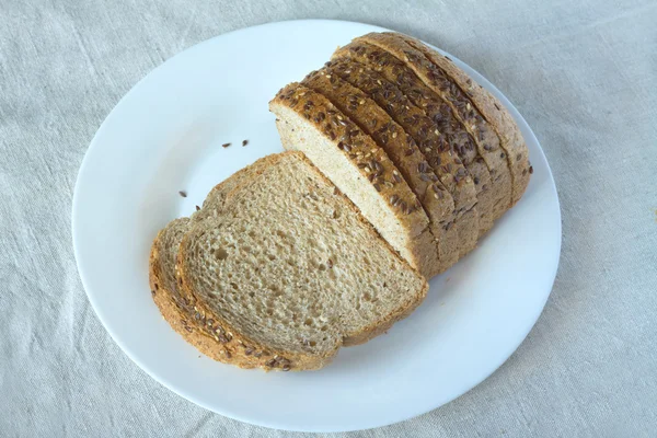 Pane di grano affettato con sesameon piatto bianco su tovaglia grigia — Foto Stock