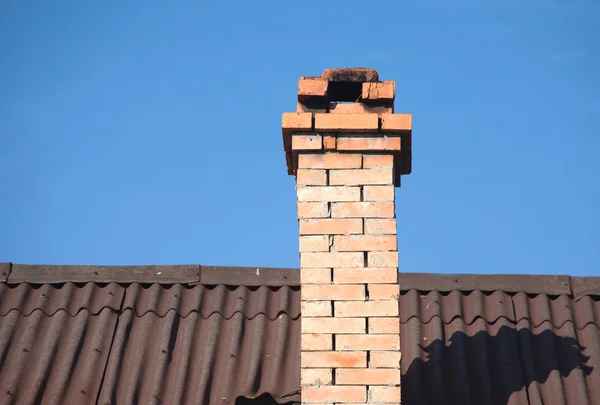 Roof of rural house with old smoke pipe from bricks over blue cloudless sky — Stock Photo, Image