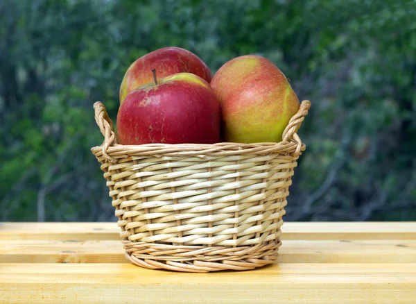 Maçãs em cesta de vime marrom claro na mesa de madeira — Fotografia de Stock