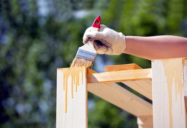Vrouwelijke hand verven bruin een houten meubilair buitenshuis close-up — Stockfoto