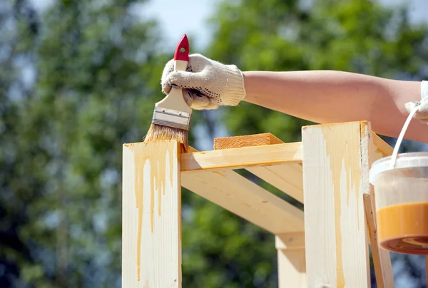 Vrouwelijke hand schildert bruin een houten rekken buitenshuis close-up — Stockfoto