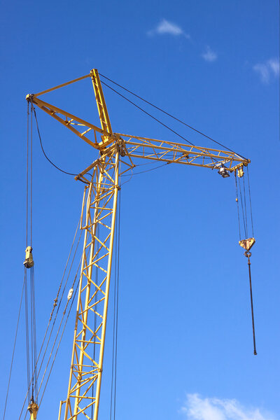 Tower construction crane over clear blue sky with light white clouds