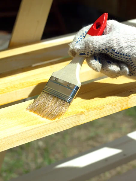 Female hand in textile glove paint wooden shelving outdoors — Stock Photo, Image