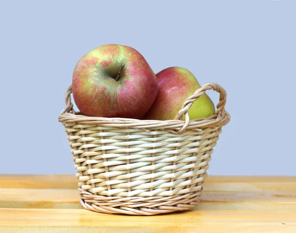 Apples in light brown wicker basket on wooden table — Stock Photo, Image