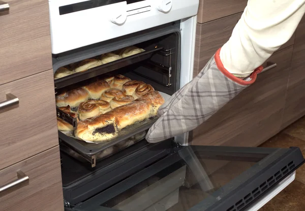 Hostess membuka pintu oven dan mengambil bakery dari kompor dapur. Tampilan samping close-up — Stok Foto