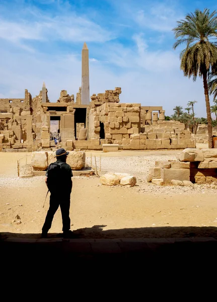 リュクソールのエジプトの寺院の遺跡の背景にバックパックと帽子を持つ典型的な観光客のシルエット エジプトへの観光と古代文化への旅行 — ストック写真