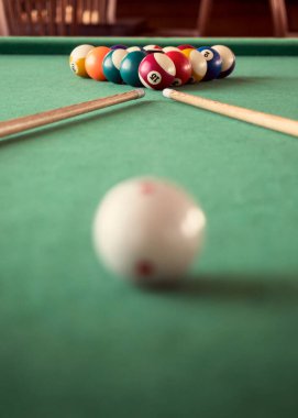 Bilardo ıstakaları ve renkli bilardo topları bir oyun masasına odaklanmış, bilardo oynamak için yıllanmış ekipmanlar. Bilardo kulübünde bilardo masasında ön planda bulanık bir bilardo topuyla oynanıyor..