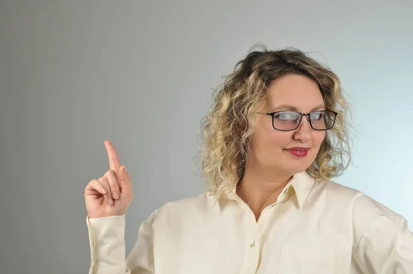 Sarı saçlı, beyaz bluzlu, gözlüklü genç bir kadın.