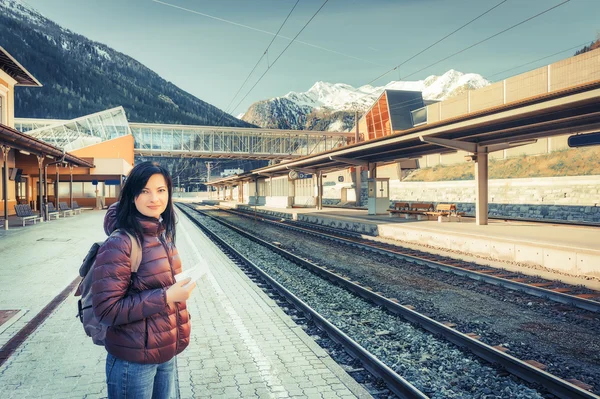 Travel by train on the Baltic railway. Girl waiting train on the platform, in the background snow-capped mountains.