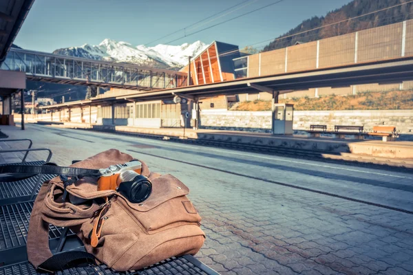 Подорожі на поїзді в альпійському залізниці. Камера і рюкзак лежачими на лавці біля залізничного вокзалу переглядів над на засніжені гори — стокове фото
