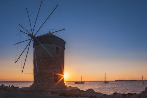 Mill on the background of the rising sun in the harbor of Mandraki. Rhodes Island. Greece