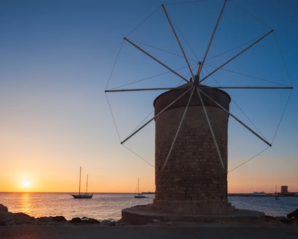 Mill on the background of the rising sun in the harbor of Mandraki. Rhodes Island. Greece