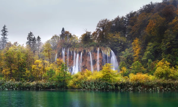 Croacia. Plitvice Lakes. Cascada panorámica en tiempo lluvioso con árboles otoñales y cielos grises — Foto de Stock