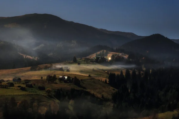 Montanhas Cárpatas. Noite de luar nas montanhas, a aldeia na colina no nevoeiro — Fotografia de Stock