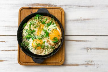 Çırpılmış yumurta, yeşil lahanalı ve yeşil soğanlı ahşap arka planda bir tavada..