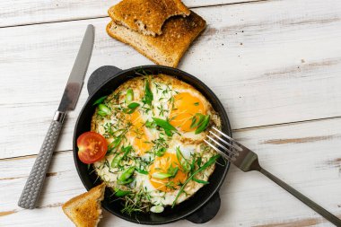 Çırpılmış yumurta, yeşil lahanalı ve yeşil soğanlı ahşap arka planda bir tavada..