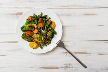 Beyaz ahşap arka planda tabakta çeşitli kızarmış sebzeler. Havuç, yeşil fasulye ve karnabahar karışımı..