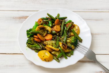 Beyaz ahşap arka planda tabakta çeşitli kızarmış sebzeler. Havuç, yeşil fasulye ve karnabahar karışımı..