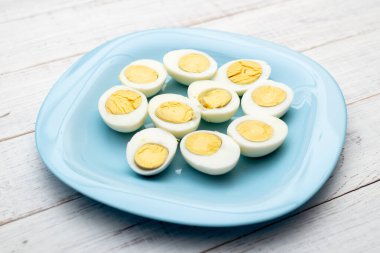 Haşlanmış yumurta, beyaz ahşap arka planda mavi bir tabakta ikiye bölünmüş..