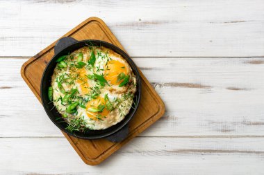 Çırpılmış yumurta, yeşil lahanalı ve yeşil soğanlı ahşap arka planda bir tavada..