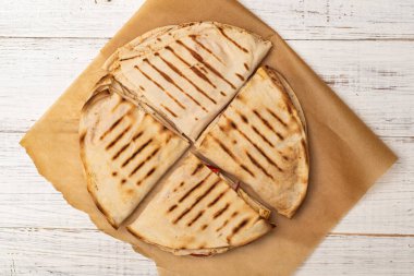 Pita, beyaz ahşap arka planda peynirli ve jambonlu tortilla. Hafif, sağlıklı bir atıştırmalık.