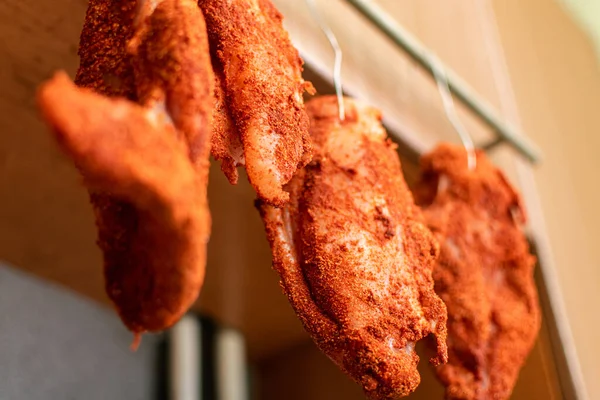 Pieces of meat in seasoning hang on hooks. Drying chicken meat, curing meat.