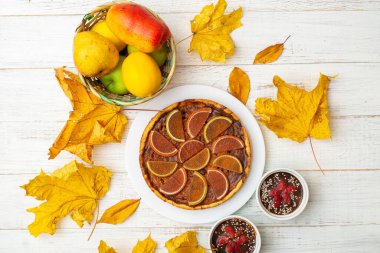 Beyaz ahşap arka planda balkabağı turtası. Sarı sonbahar yaprakları, elmalar ve armutlar.