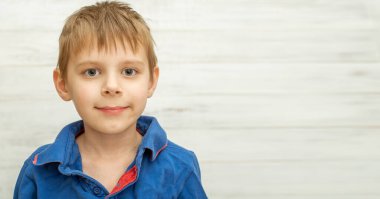 6-8 yaşlarında bir çocuk gülümser ve dik bakar..