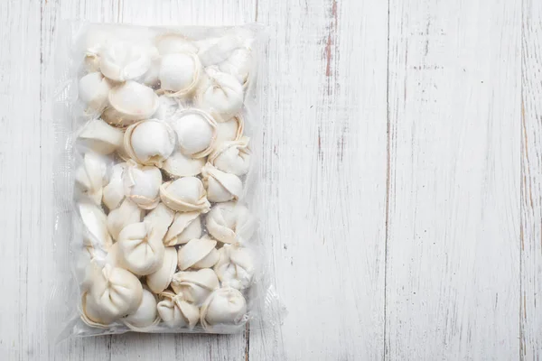 Beyaz ahşap arka planda paketlenmiş donmuş hamur köfteleri..