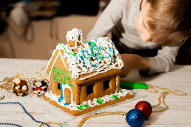 Bir çocuk zencefilli kurabiye evi dekore ediyor. Noel ve Yeni Yıl için Hazırlık.