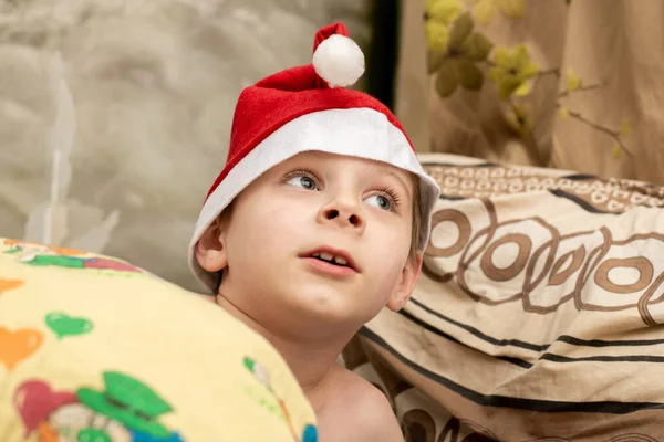 ベッドの中でサンタの帽子で驚くべき少年 奇跡のクリスマスの期待 — ストック写真