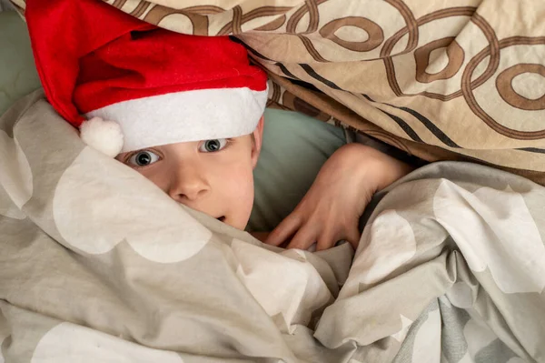 満足し 笑顔の少年はサンタの帽子にベッドに横たわっている 休日の喜びの感じ クリスマス — ストック写真