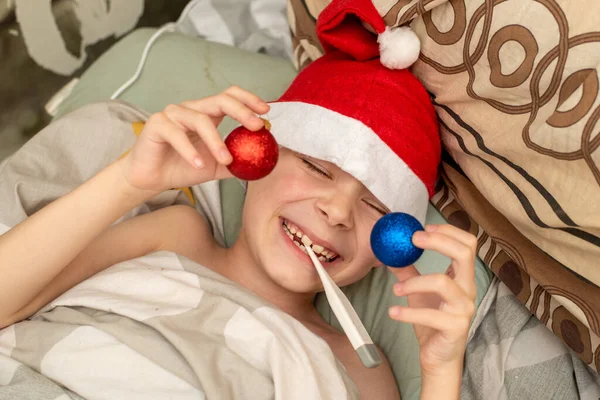 サンタの帽子の少年は病気です ベッドの温度を測定します 新年の病気 — ストック写真