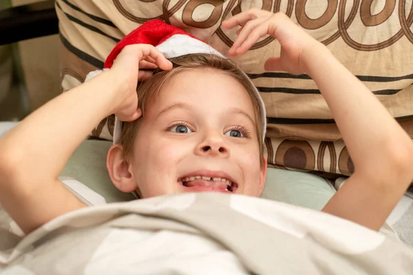 満足し 笑顔の少年はサンタの帽子にベッドに横たわっている 休日の喜びの感じ クリスマス — ストック写真