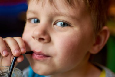 Küçük çocuk bir kafede pipetten kokteyl içiyor..